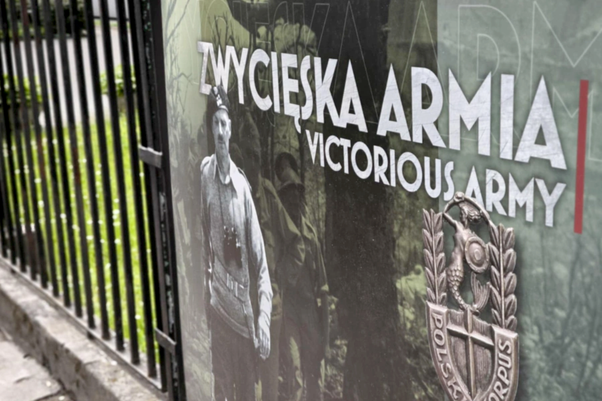 Fragment wystawy na czarnym płocie z białym tekstem "ZWYCIĘSKA ARMIA | VICTORIOUS ARMY", wizerunkiem żołnierza w mundurze oraz emblematem z tarczą i figurą syrenki, na zielonym tle.